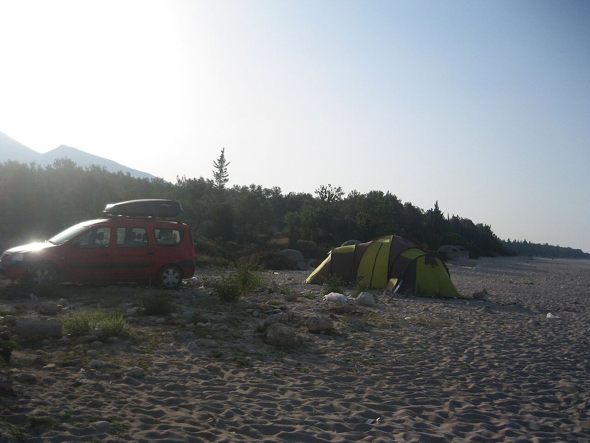 Šator postavljen na šljunčanoj plaži uz mirno more i planine
