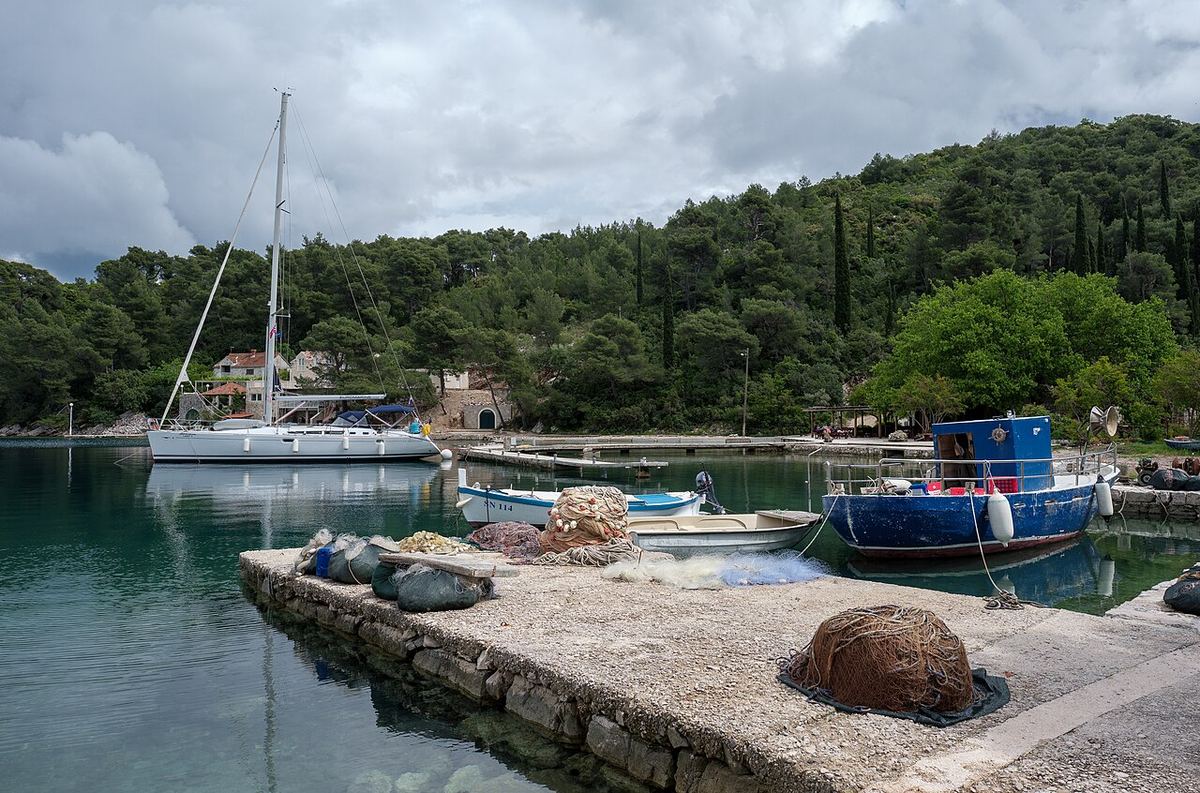 Jedrilica i ribarski brod privezani u mirnoj uvali okruženoj borovima